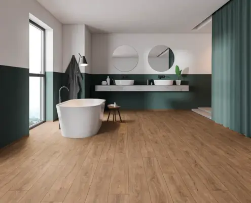 Baño moderno con suelo de madera y bañera independiente junto a una ventana grande. Decoración en tonos verde oscuro y blanco, con doble lavabo y espejo redondo en la pared.